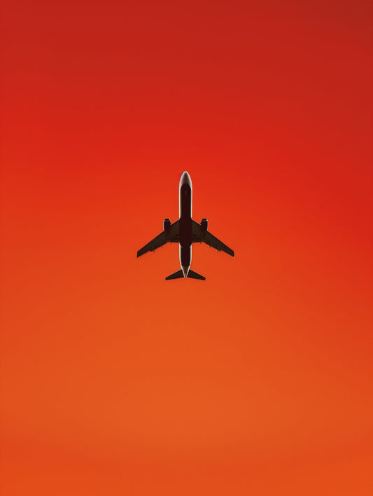 Airplane silhouette flying against a vivid red-orange sunset sky.